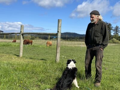 Man standing next to his black and white dog on farm